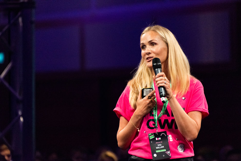Woman in a pink t-shirt talking at a conference holding a microphone