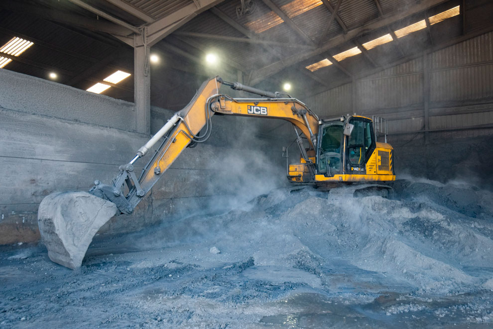 Large yellow digger working on top of a pile of grey metal powder