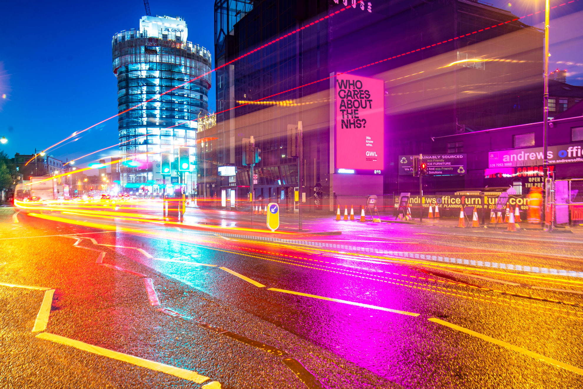 Dramatic night time shot of a busy city street with a prominent, pink illuminated billboard.