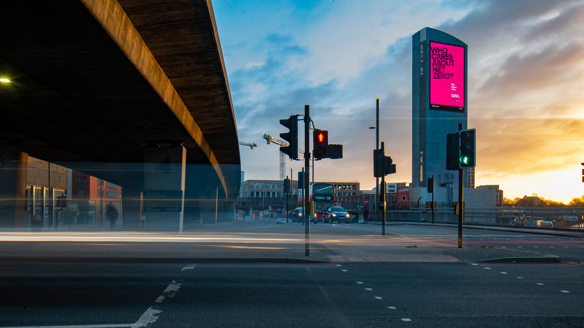 Sunrise shot of a large, illuminated billboard by the side of a road.