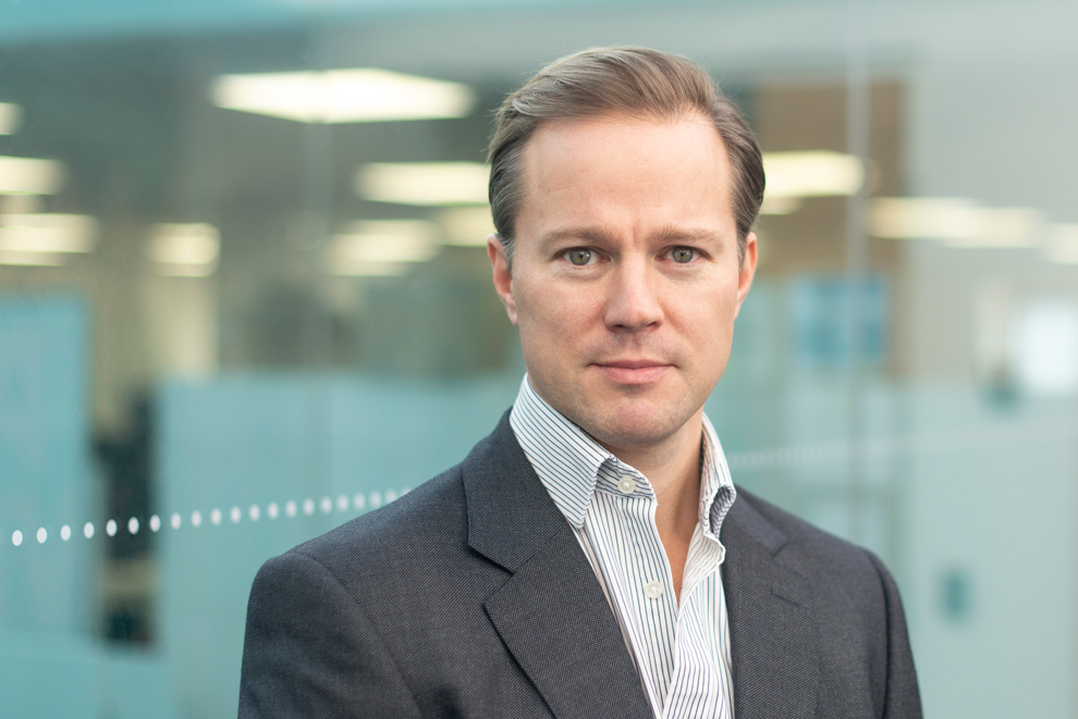 Confident man in light shirt photographed in glass office setting, modern business headshot
